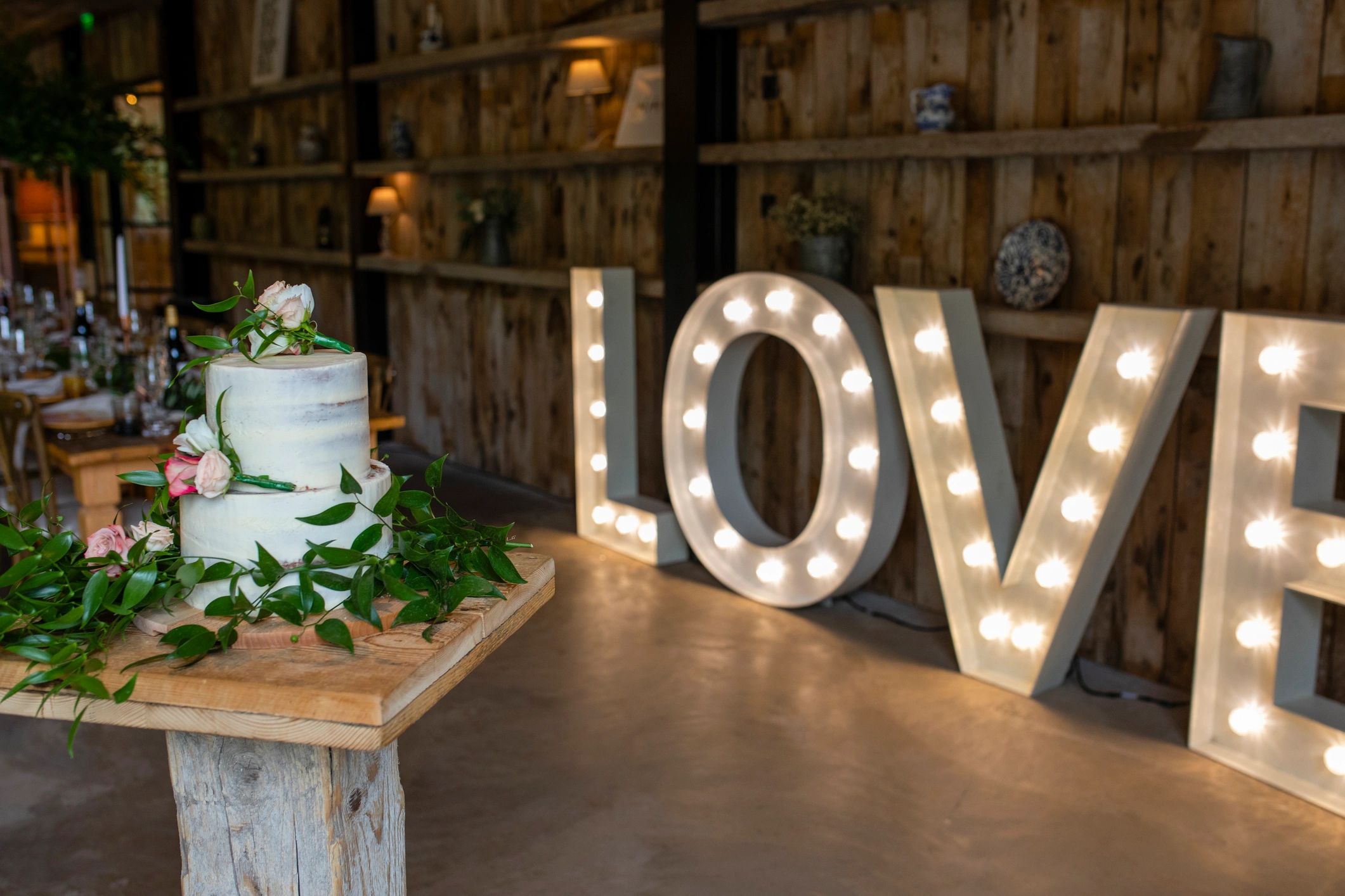 Wedding cake display at a reception with illuminated letters in the background