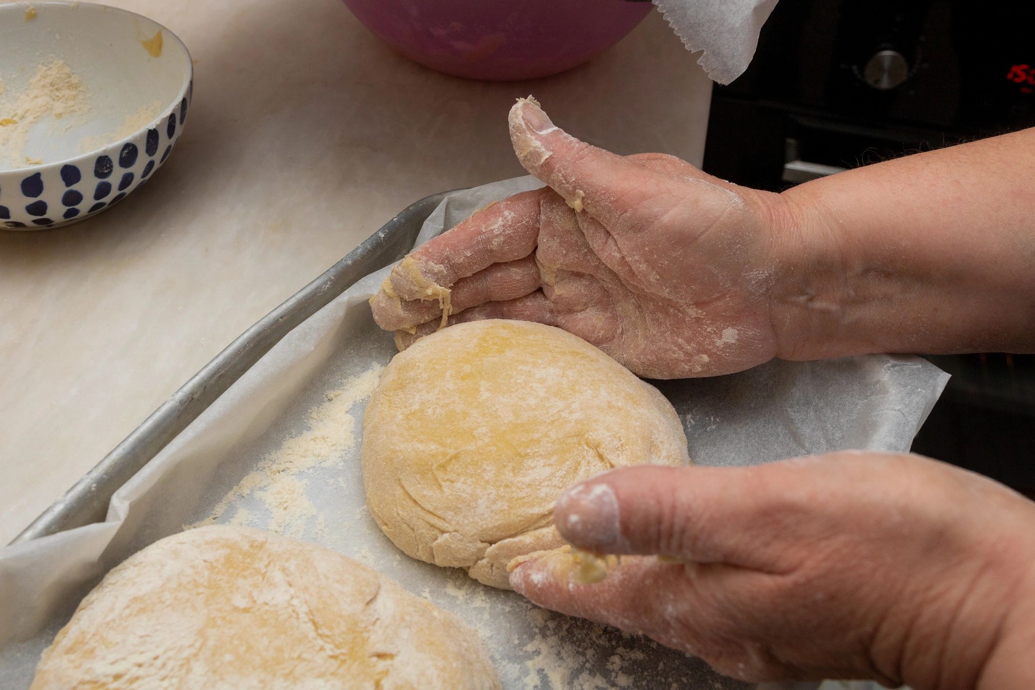 Hands shaping bread dough on a floured tray